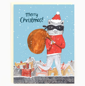 A sky blue card with a raccoon dressed as Santa wearing a robber's mask while holding a brown sac, walking across the roof of a house. In the background there are other houses..