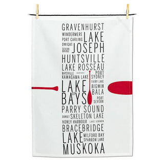 White tea towel with black text in a row down the middle listing Muskoka lake names with a red canoe oar.