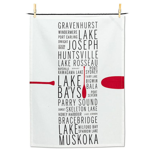 White tea towel with black text in a row down the middle listing Muskoka lake names with a red canoe oar.