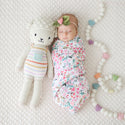 A sleeping baby in a floral swaddle and headband sleeping next to the larger doll