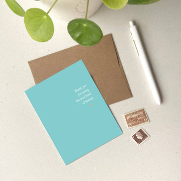 Best Kind of Human Card - Blue greeting card with white text "Best kind of human you already are" beside brown envelope and white pen on white surface