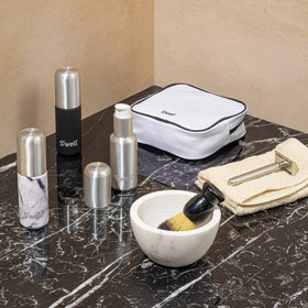Onyx Travel Bottle Set - Black, white, and silver sleek travel bottles with marble and matte finishes next to a white zippered travel pouch and.