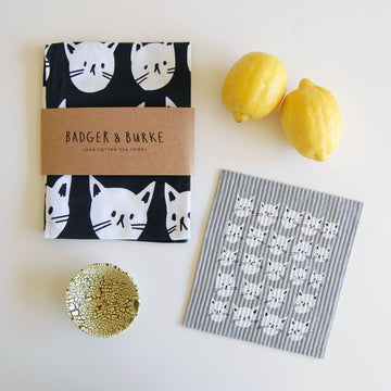 Many Cats Sponge Cloth - Black and white tea towel with playful cat faces and a striped, cat-patterned sponge cloth, paired with yellow lemons and a.