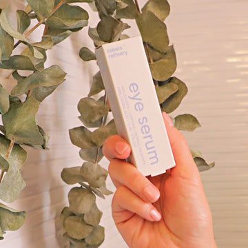Eye Roller Serum  Brighten/Soften/Moisturize - Hand holding a white box of Rebel's Refinery eye roller serum, with green eucalyptus leaves, unique Canadian handmade gift.