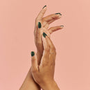 Vegan & 21-free Nail Polish - En Beau Fusil - Hands with dark green vegan nail polish on natural nails against a soft pink background, showcasing unique, handmade.
