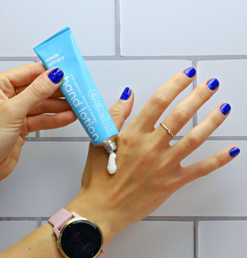 Hand lotion - ALMOND HONEY - Light blue tube of hand lotion with white text dispensing cream on hand with blue nail polish and pink watch.