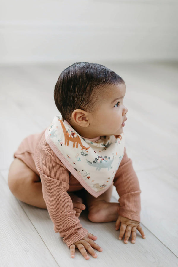 A baby wearing the baby dinomite bandana bib (pink bib with the dinosaurs and flowers