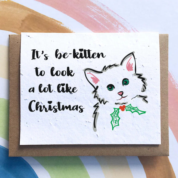 A white card with a cat on the right hand side wearing a Christmas wreath collar with the words phrase "It's be-kitten to look a lot like Christmas"