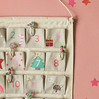 A canvas advent calendar with 24 pockets with holiday themed designs on each day. The calendar is hanging on a pink wall with stars