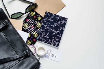 Thanks Vines Card - Black greeting card with white vine illustrations and handwritten-style "Thank you!" text, standing among accessories.