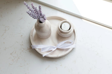 Lynn & Liana Fluted Round Tray - Round fluted ceramic tray in soft beige holding a textured vase with lavender and a small white candle holder with ribbon.
