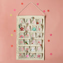 A canvas advent calendar with 24 pockets with holiday themed designs on each day. The calendar is hanging on a pink wall with stars