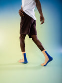 A model wearing the socks while walking away from the camera; the socks are beige with a blue stripe down the back and underneath the foot