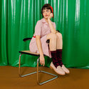 A model sitting on a chair in front of a green backdrop, staring off to the side while modelling the socks