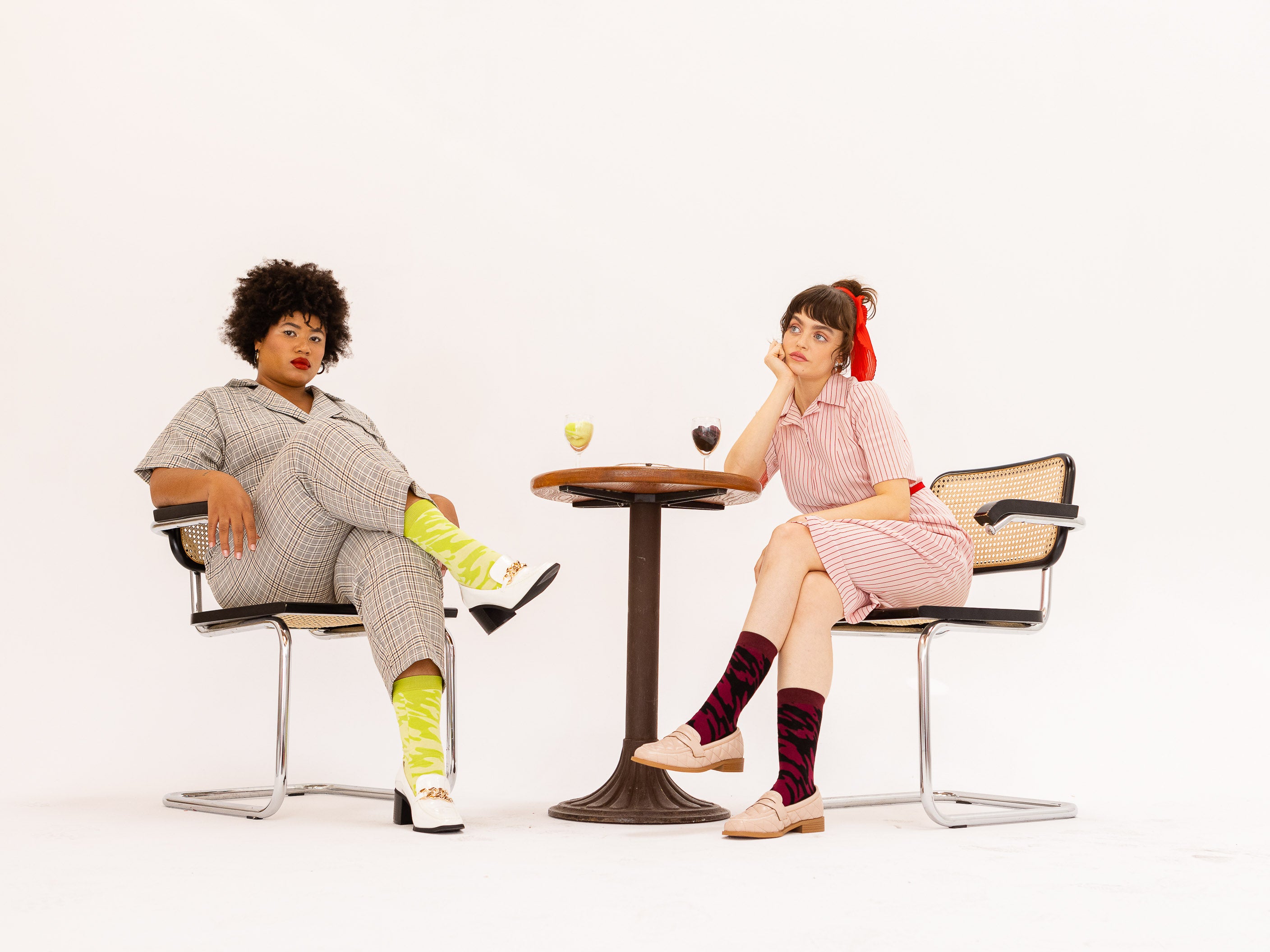 Two models wearing the red wine and white wine versions of the socks while sitting at a table together, drinking their respective wines