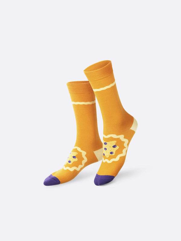 Light brown socks with purple toes, a cream heel and a splatter covered with blueberries in the middle of the sock