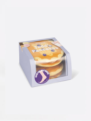 A purple box with a clear panel to display light brown socks folded to resemble a stack of pancakes with blueberries on them