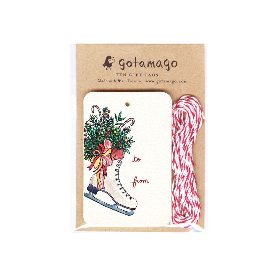 A white gift tag with a white skate filled with holly, pine and candy canes next to red font reading "to" and "from". Next to the gift tags is red and white twine.