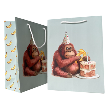 Go Bananas Gift Bag - Light blue gift bag with playful orangutan wearing a party hat, holding a banana next to a birthday cake, white rope.