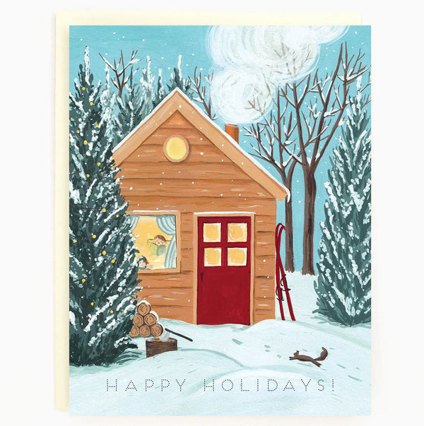 A card with an illustration of a cottage in a wintry forest with a red door, a pair of red skis leaning on the side and an axe next to a pile of wood logs. At the bottom of the card reads 