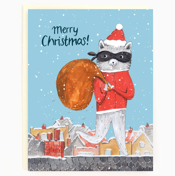 A sky blue card with a raccoon dressed as Santa wearing a robber's mask while holding a brown sac, walking across the roof of a house. In the background there are other houses.. 