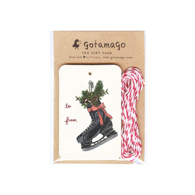 A white gift tag with a black skate filled with holly, a pinecone and a candy cane next to red font reading "to" and "from". Next to the tags are red and white twine.