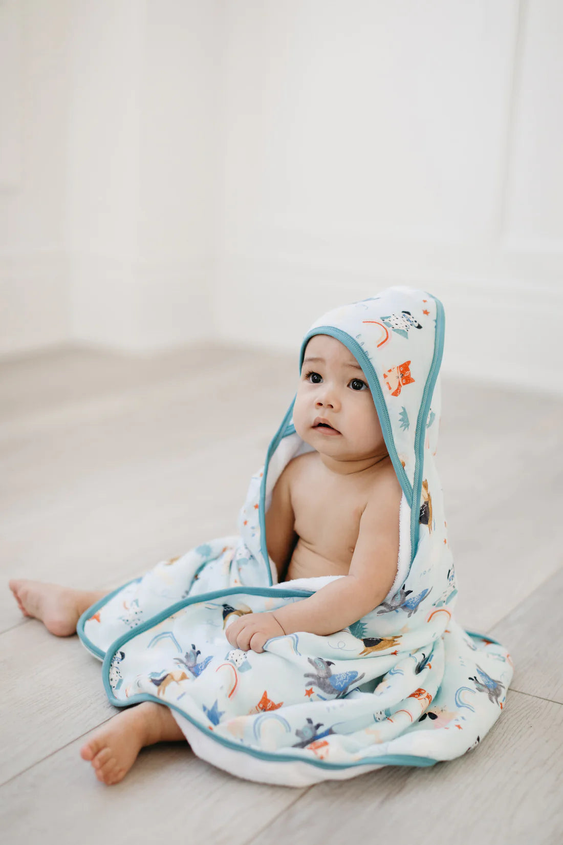 A baby wearing a hooded towel with superhero dogs and shooting stars