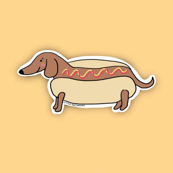 A dachshund dog in a hot dog bun and ketchup and mustard on it's back
