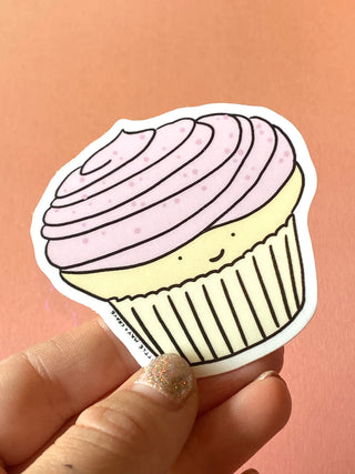 A sticker shaped like a cupcake. The cupcake has light pink icing with pink sprinkles and a white cake base