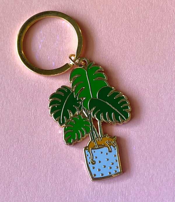 A keychain of a brown cat sitting on a blue potted fern.