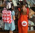2 girls standing side by side, the one on the left is wearing the cherry check rucksack while the one on the right is wearing the cherry bag