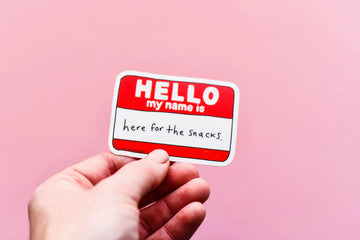 Here for the Snacks Vinyl Sticker - Hand holding a handmade vinyl sticker with red and white "Hello my name is" label saying "here for the snacks," unique.