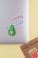 The avocado sticker on the corner of a grey laptop. In the corner there is another sticker still in the package