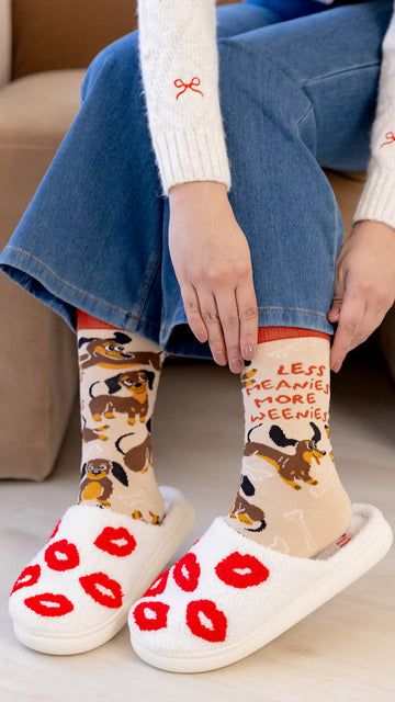 Women's Meanie Weenie Socks - Handmade Canadian women's socks with dog print and red text "Less Scary More Cozy" paired with white slippers featuring red.