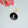 A black circle on a keychain with the letter F in the middle