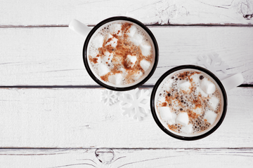Merry Christmoose Hot Chocolate Pouch - Two white mugs with black rims filled with hot chocolate, topped with marshmallows and sprinkled cocoa, on a rustic white.
