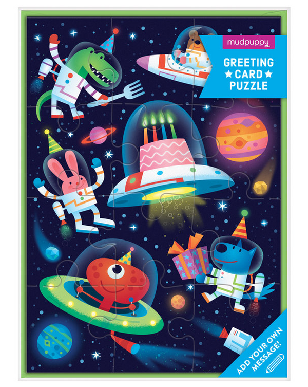 A dark navy puzzle card with animals and aliens in space suits floating around a birthday cake inside a space capsule