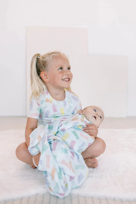 A kid wearing a gummy bear PJ set holding a baby in a swaddle with the same gummy bear pattern