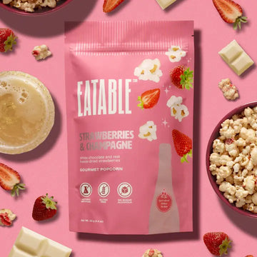 Strawberries & Champagne - Gourmet Popcorn - Pink bag of Strawberries & Champagne gourmet popcorn with scattered fresh strawberries and white chocolate pieces, Canadian.