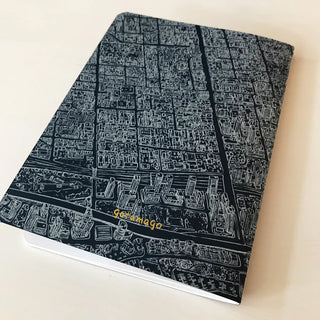 A black notebook with a detailed, fine-line white illustration of Toronto from a birds-eye view. A removable label sleeve reads 