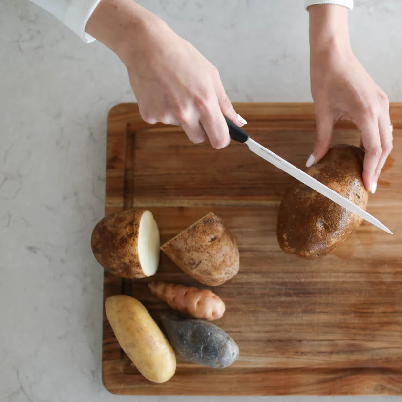 An overhead view of a wood chopping board and someone chopping up potatoes 