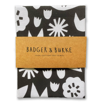 June Floral Tea Towel - Black cotton tea towel with white stylized floral patterns, wrapped with a brown paper band labeled Badger & Burke.