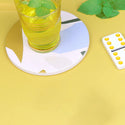Coaster shown up close with a glass of lemonade on it next to a yellow domino