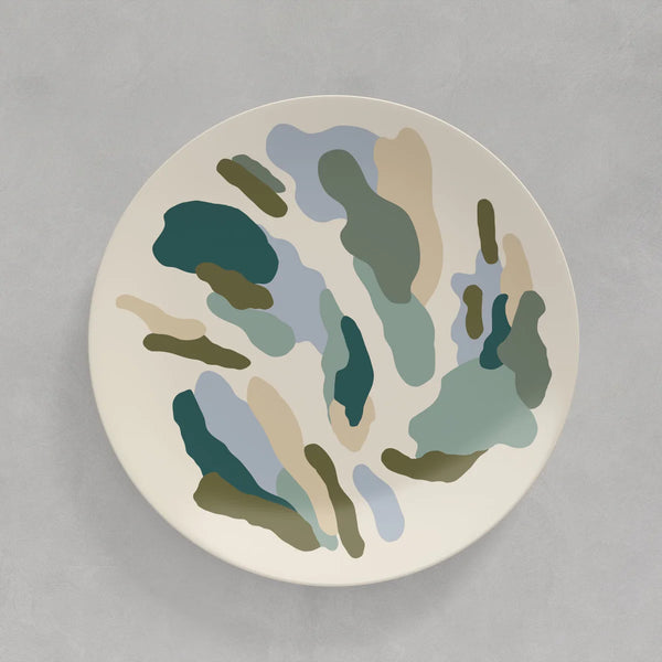 A cream coloured plate with abstract splashes of olive green, light blue, turquoise and cream against a grey background