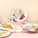1 plate and 1 coaster leaning against a pastel yellow wall. In front there are 3 coasters stacked on each other, 2 plates stacked each other and a plate half covered by a dish towel