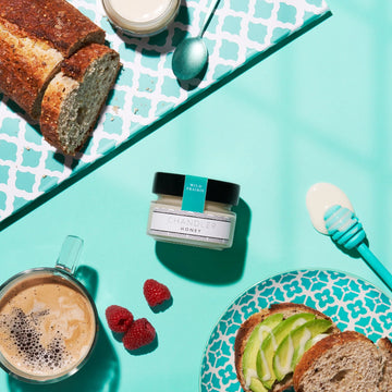 Classic Wild Prairie Honey (Chandler Honey) - Small jar of handmade Canadian wild prairie honey with honey dipper, bread, raspberries, and coffee on turquoise background.
