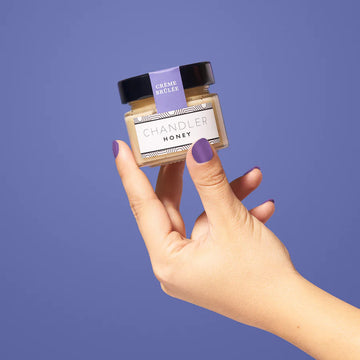Créme Brûlée (Chandler Honey) - Hand holding small jar of Canadian handmade Chandler Honey Créme Brûlée gift with black lid and lavender label.