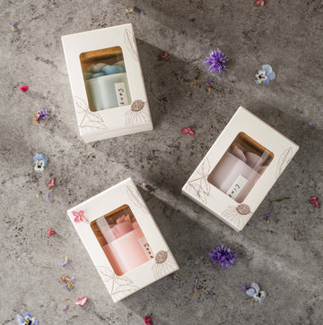 Anemone Floral Soy Candles - 8 oz: Pink - Sunday - Three boxed soy candles in pastel green, pink, and lavender with floral designs on white packaging, set on a gray surface.