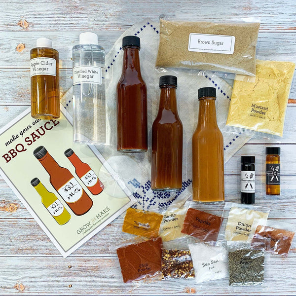  The contents (3 bottles, 2 vinegars, multiple seasoning packets, instructions, a funnel and labels) laid out on a picnic table