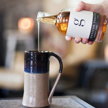 Mexican Vanilla Gourmet Coffee Syrup - Pouring golden Mexican vanilla coffee syrup from a handmade Canadian glass bottle into a ceramic mug, perfect unique gift.